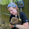 Young RVT wearing black scrubs and a floral headband holds infant american beaver at Bear Hollow Zoo